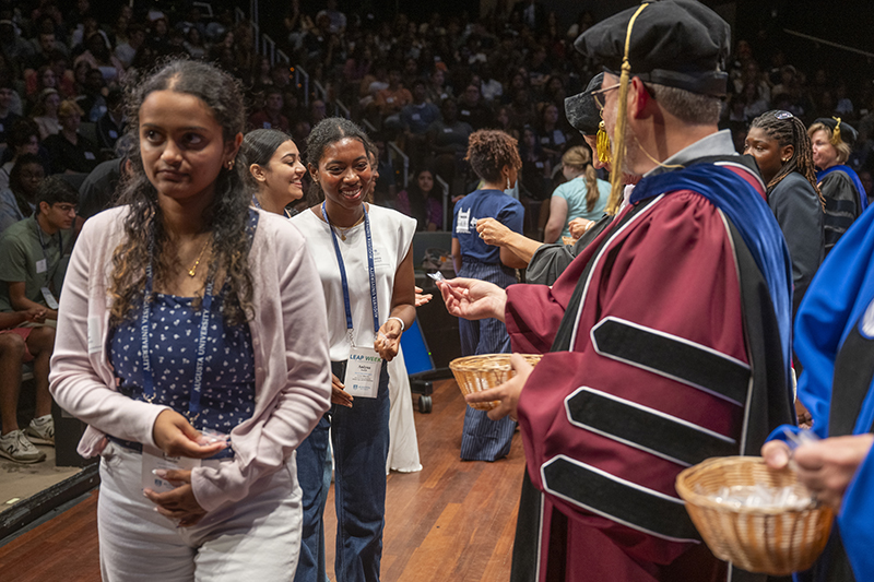 man in a graduation cap and gown handing out a pin to students