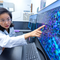 A female scientist points to a screen that shows an extreme closeup of cells in human blood.