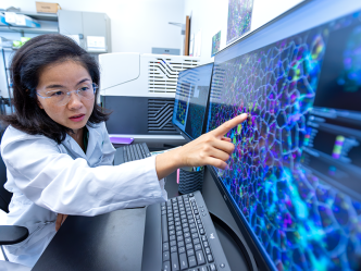 A female scientist points to a screen that shows an extreme closeup of cells in human blood.