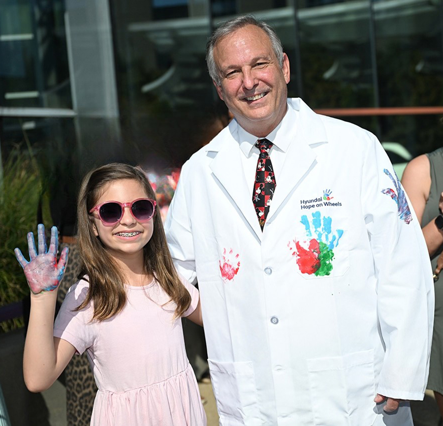 Girl holds up hand showing paint on it while standing next to a male doctor in his white lab coat