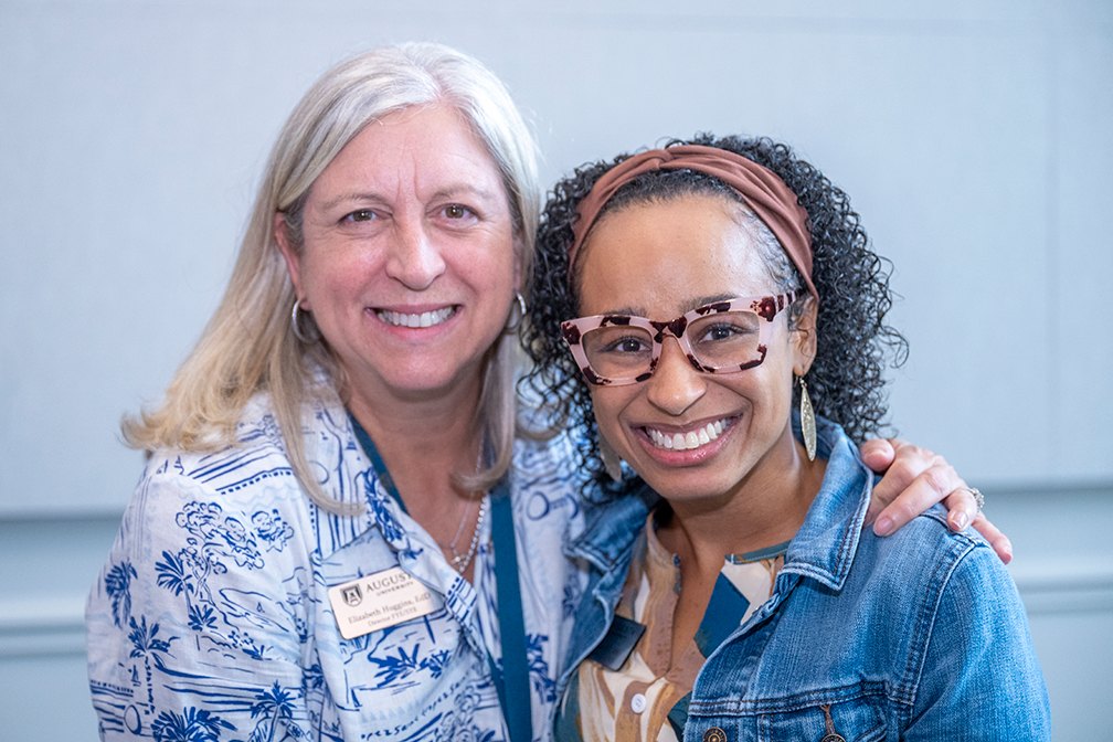 Two women smile at camera, one with arm around the shoulder