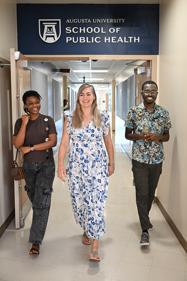 Two women and a man walk down a hallway and smile.