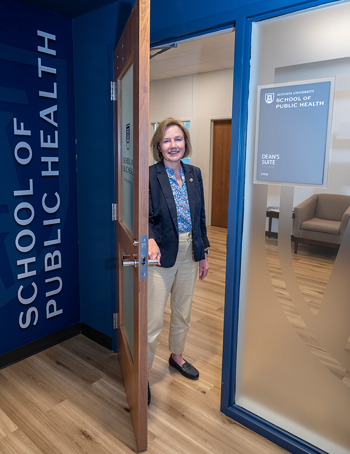 A woman wearing a suit opens a door and smiles.