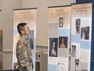 A student dressed in military gear reads a display about the history of democracy.