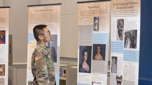 A student dressed in military gear reads a display about the history of democracy.