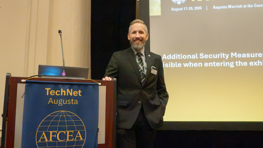 A man in a nice dark suit leaning on a podium and posing for a picture