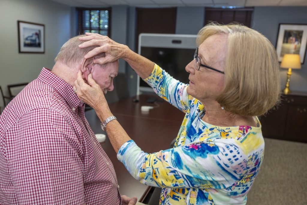 Woman attaching a prosthetic ear on her husband.