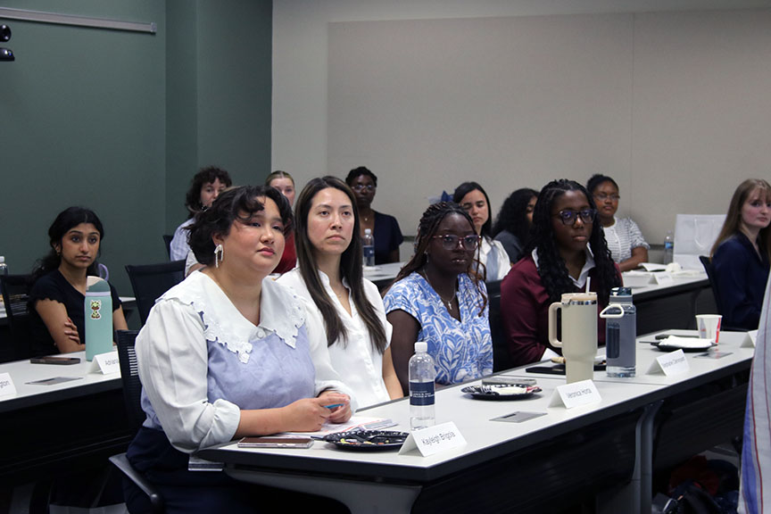 Young women sitting at a table listening to a speaker.