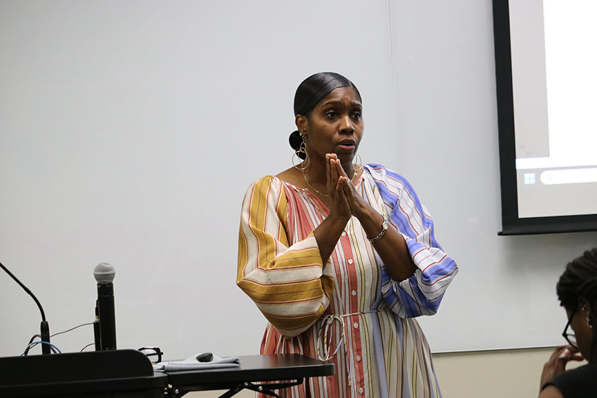 Woman stands at the front of a classroom talking.