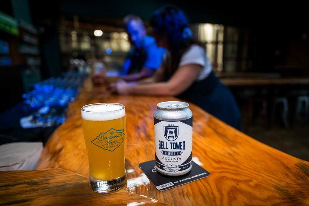a glass of beer and a can of beer with blurred people in the background