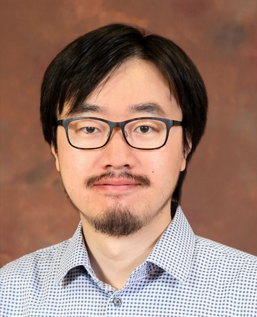 man wearing a patterned shirt and black rimmed glasses smiling