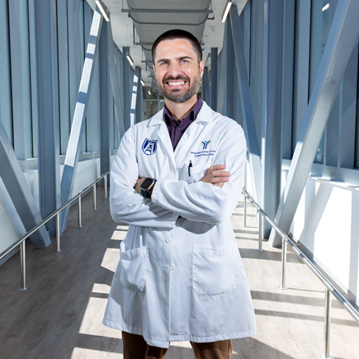 A male scientist in a laboratory coat stands in a long, modern bridge connecting two scientific labs.