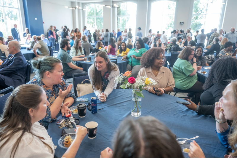 men and women sitting at round tables and standing in a room