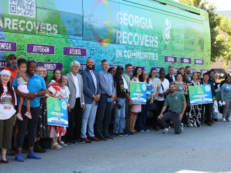 A large group of people stand in front of an addiction recovery bus and smile.