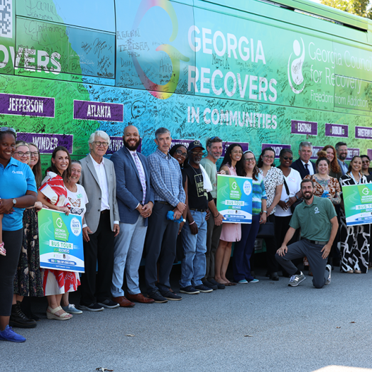 A large group of people stand in front of an addiction recovery bus and smile.