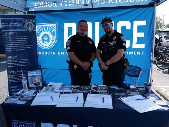Two male AUPD officers smile at the camera under a tent at an open house event.
