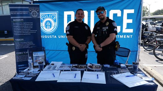 Two male AUPD officers smile at the camera under a tent at an open house event.