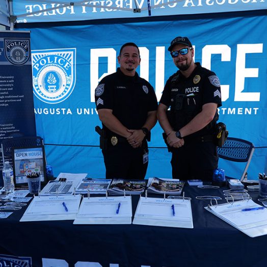 Two male AUPD officers smile at the camera under a tent at an open house event.