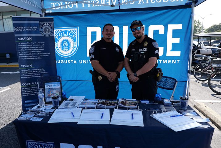 Two male AUPD officers smile at the camera under a tent at an open house event.
