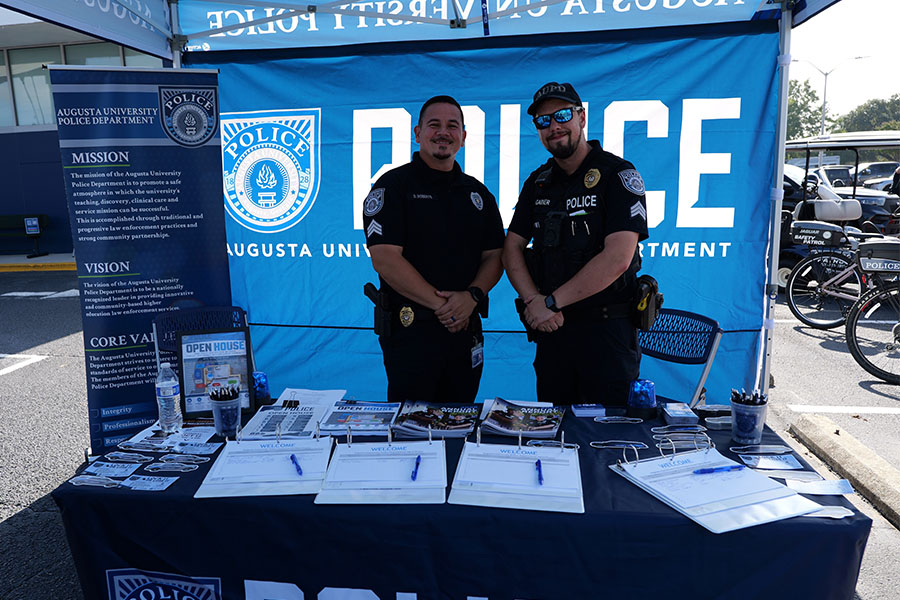Two male AUPD officers smile at the camera under a tent at an open house event.