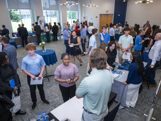 A crowd of men and women in a room talking to people behind tables
