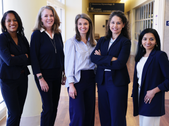 Five professionally dressed woman stand beside each other and smile.
