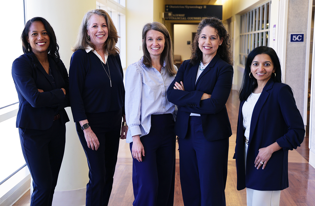 Five professionally dressed woman stand beside each other and smile.