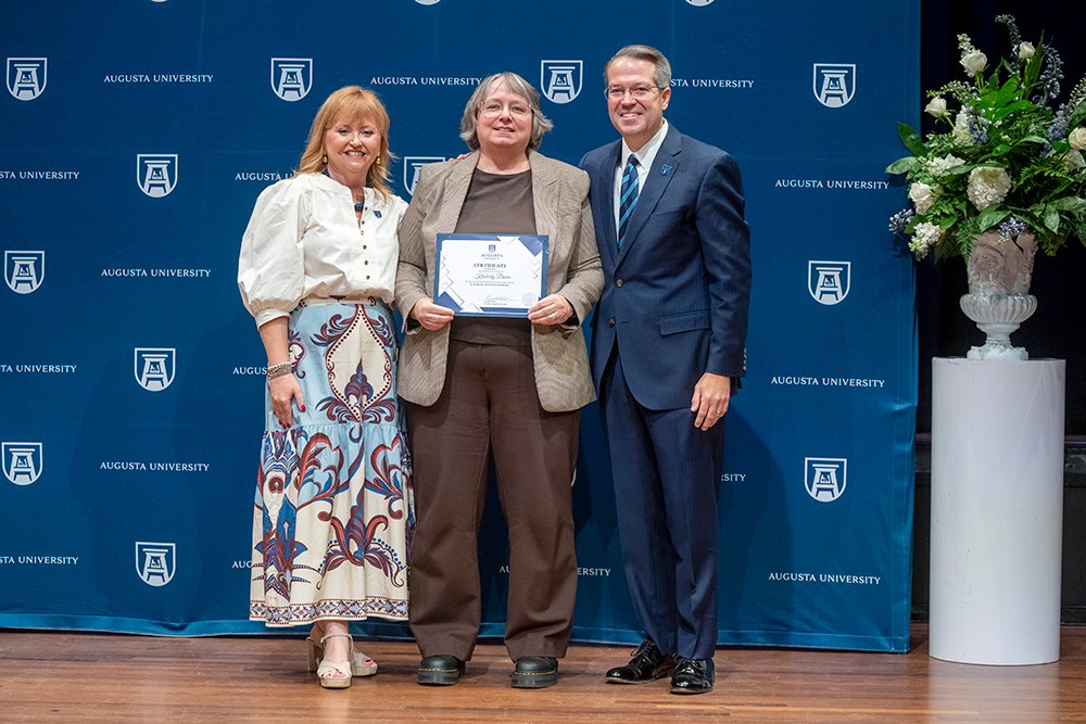 Two women and a man pose for a photo while standing in front of a blue background.