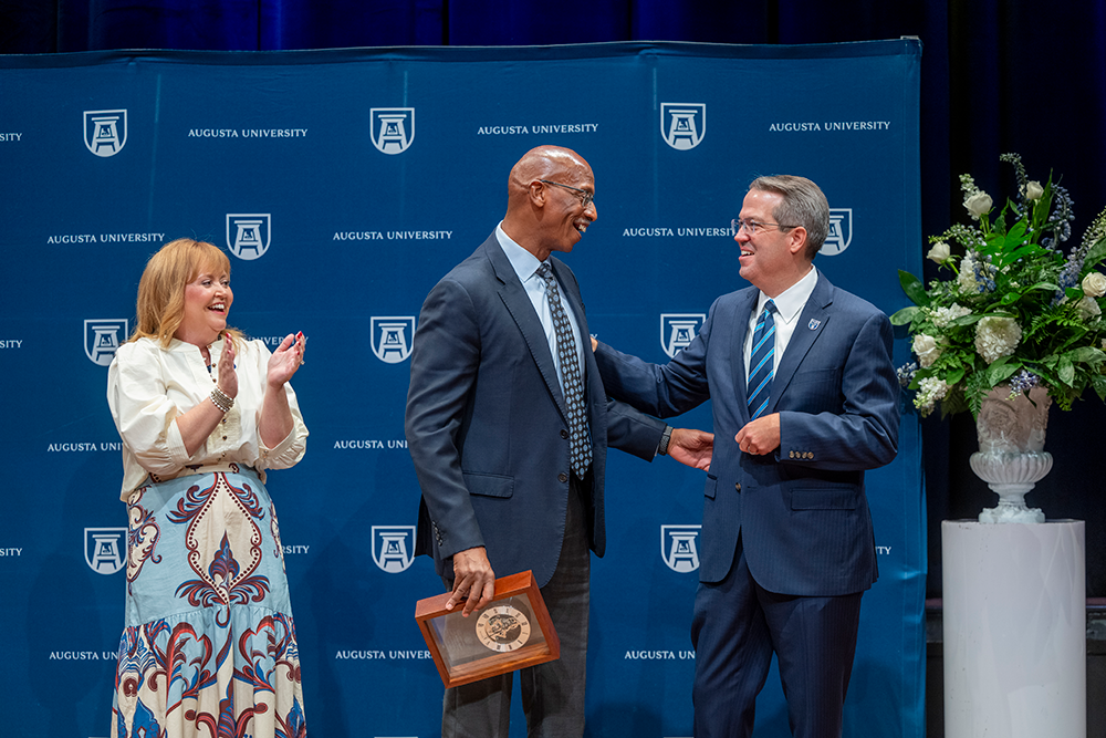 Two men smile at each other while a women claps and smiles.