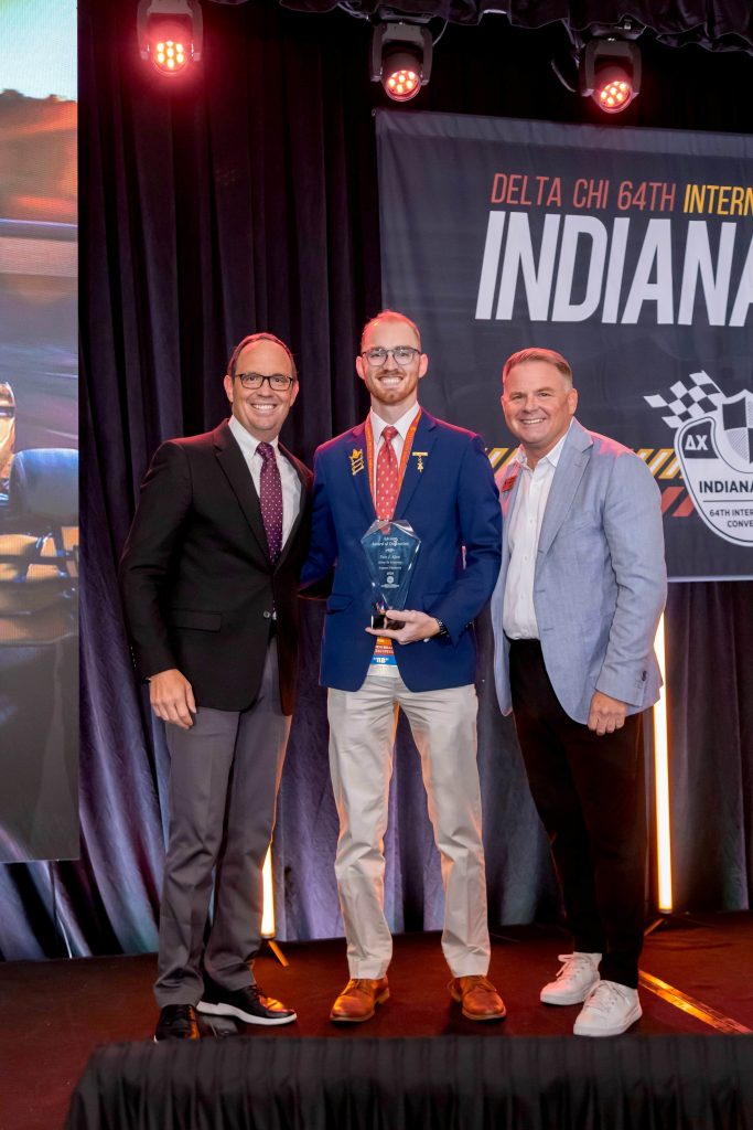 Three men smile for a photo as the man in the center holds a trophy